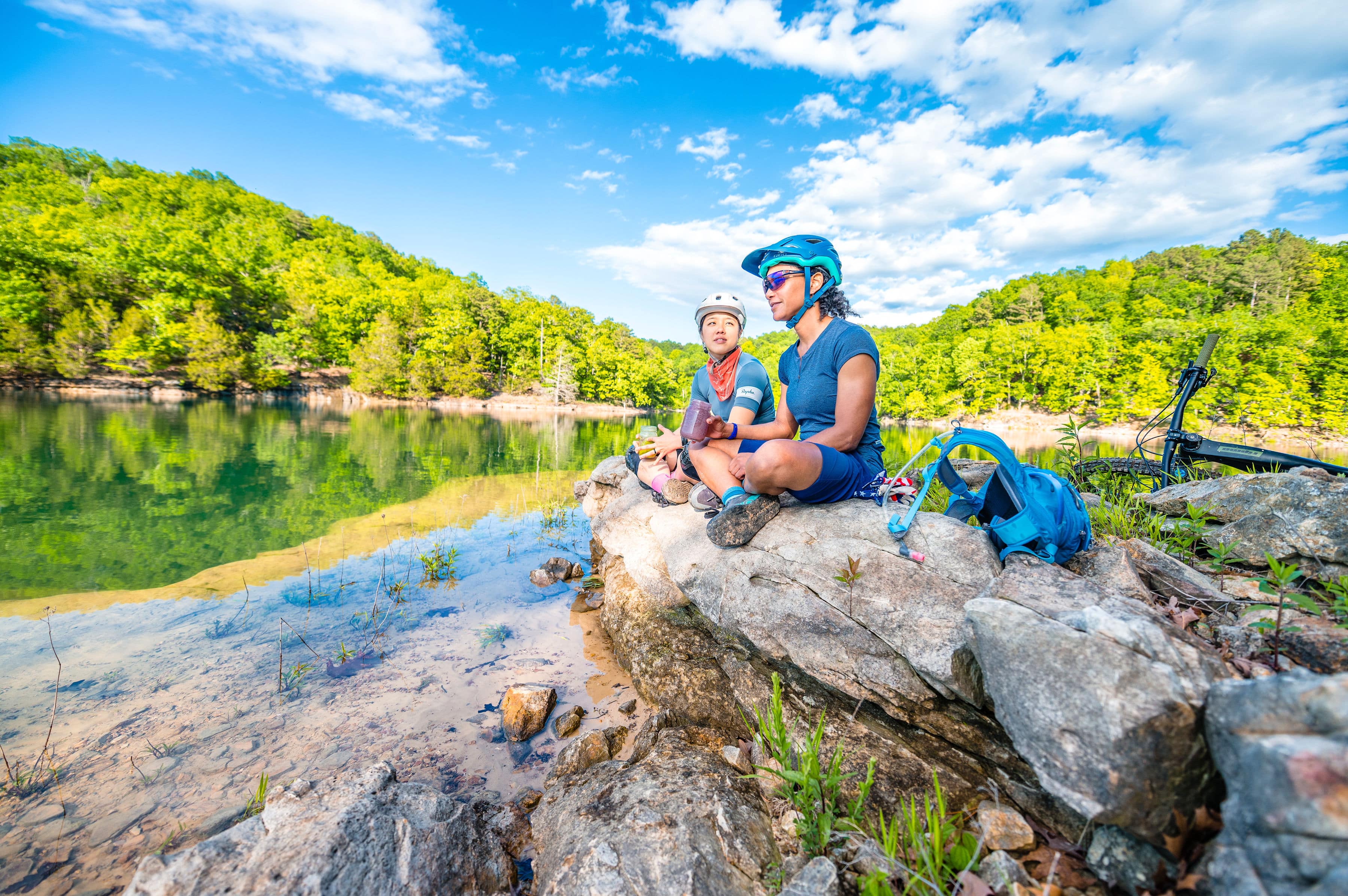 Two mountain bikers take a break sitting on a rock looking out over the water on the Monument Trails at Hobbs State Park-Conservation Area