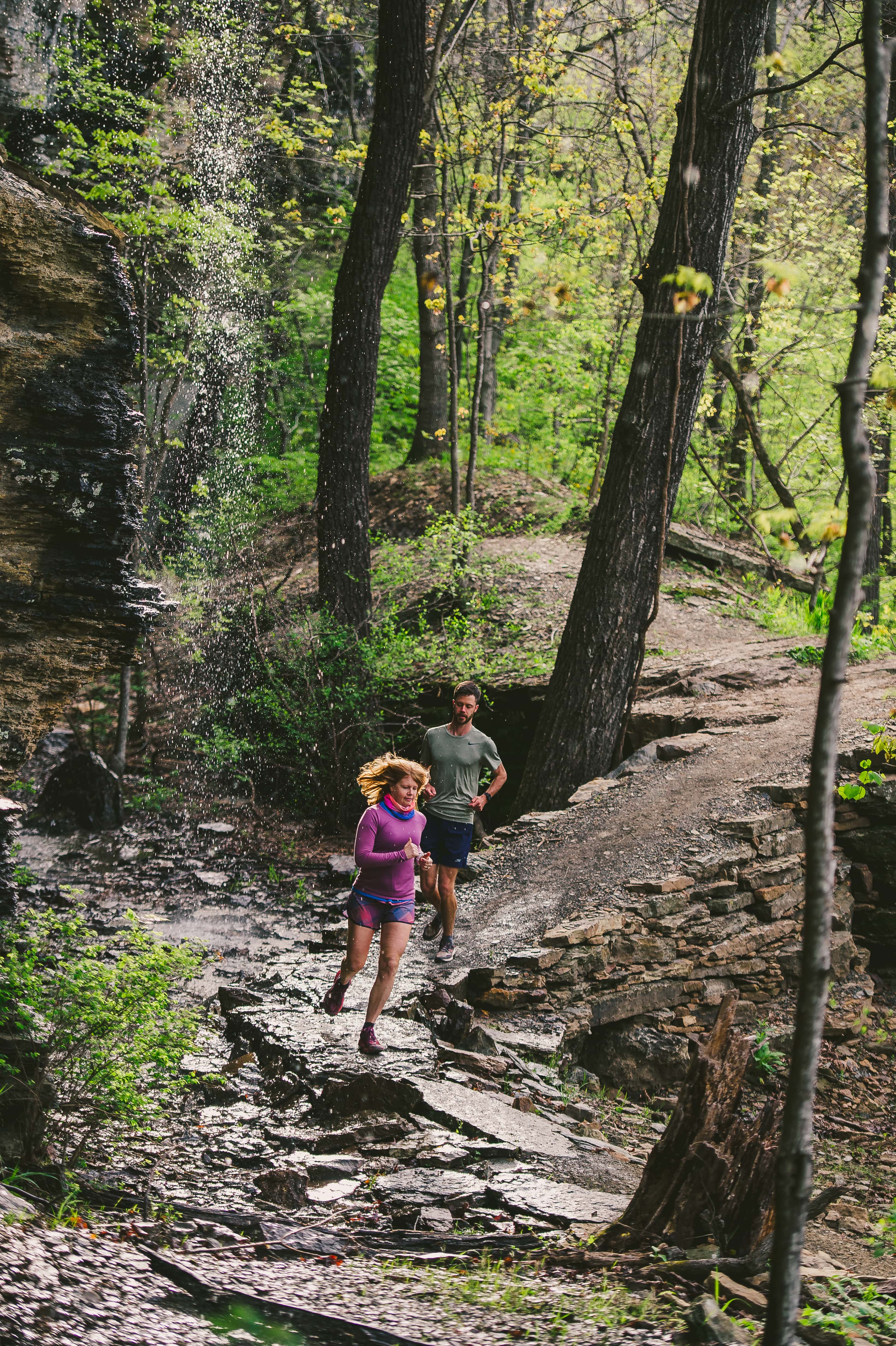 A man and woman running downhill on the Monument Trail in the Devil's Den State Park