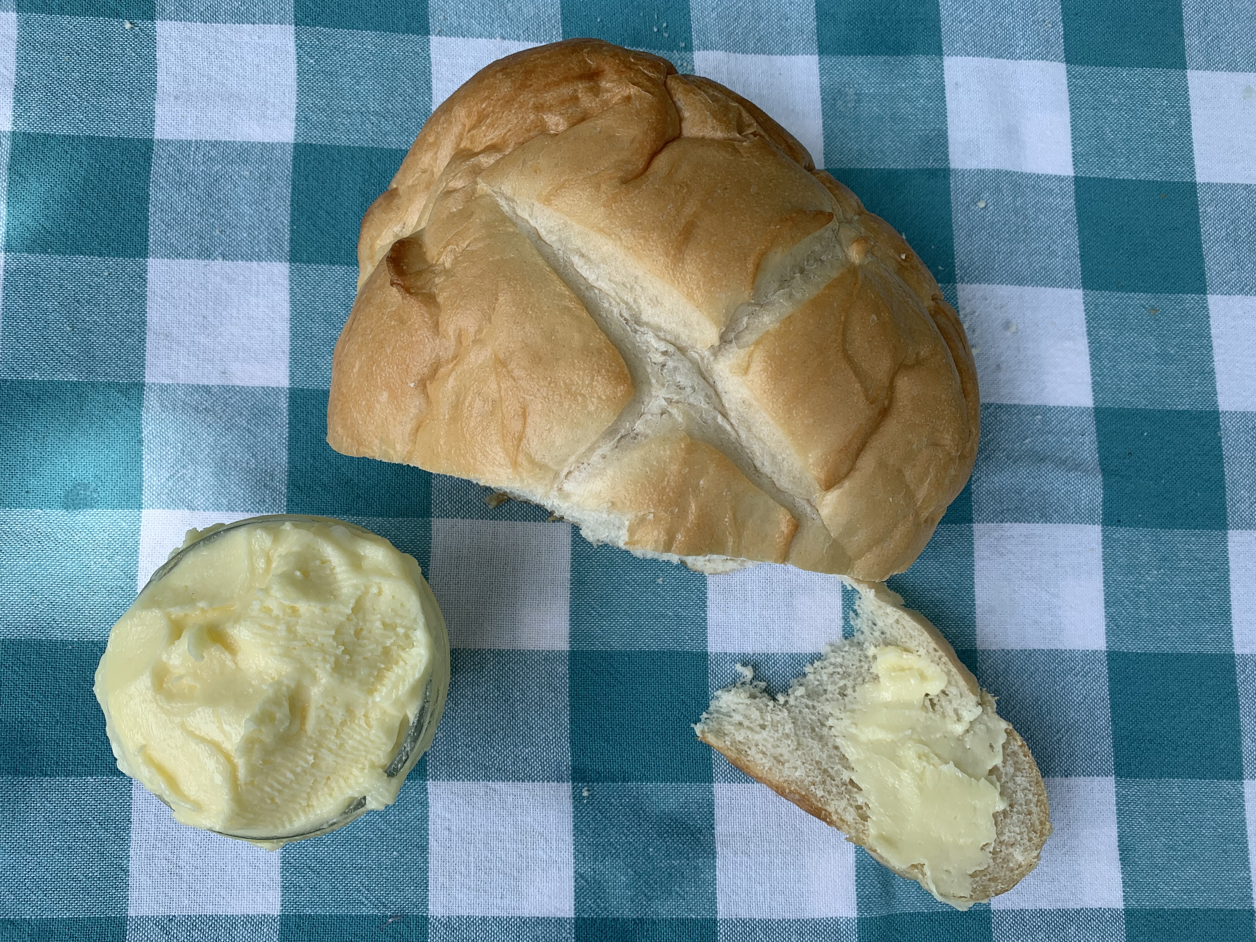 A loaf of bread on a table with a container of butter and a piece of bread off to the side with butter on it