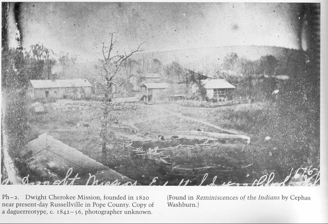 Historic black and white photo of Dwight Cherokee Mission with several buildings. Caption on images says: Dwight Cherokee Mission, founded in 1820 near present-day Russellville in Pope County. Copy of a daguerreotype, c. 1842-56, photographer unknown. [Found in Reminiscences of the Indians by Cephas Washburn.]