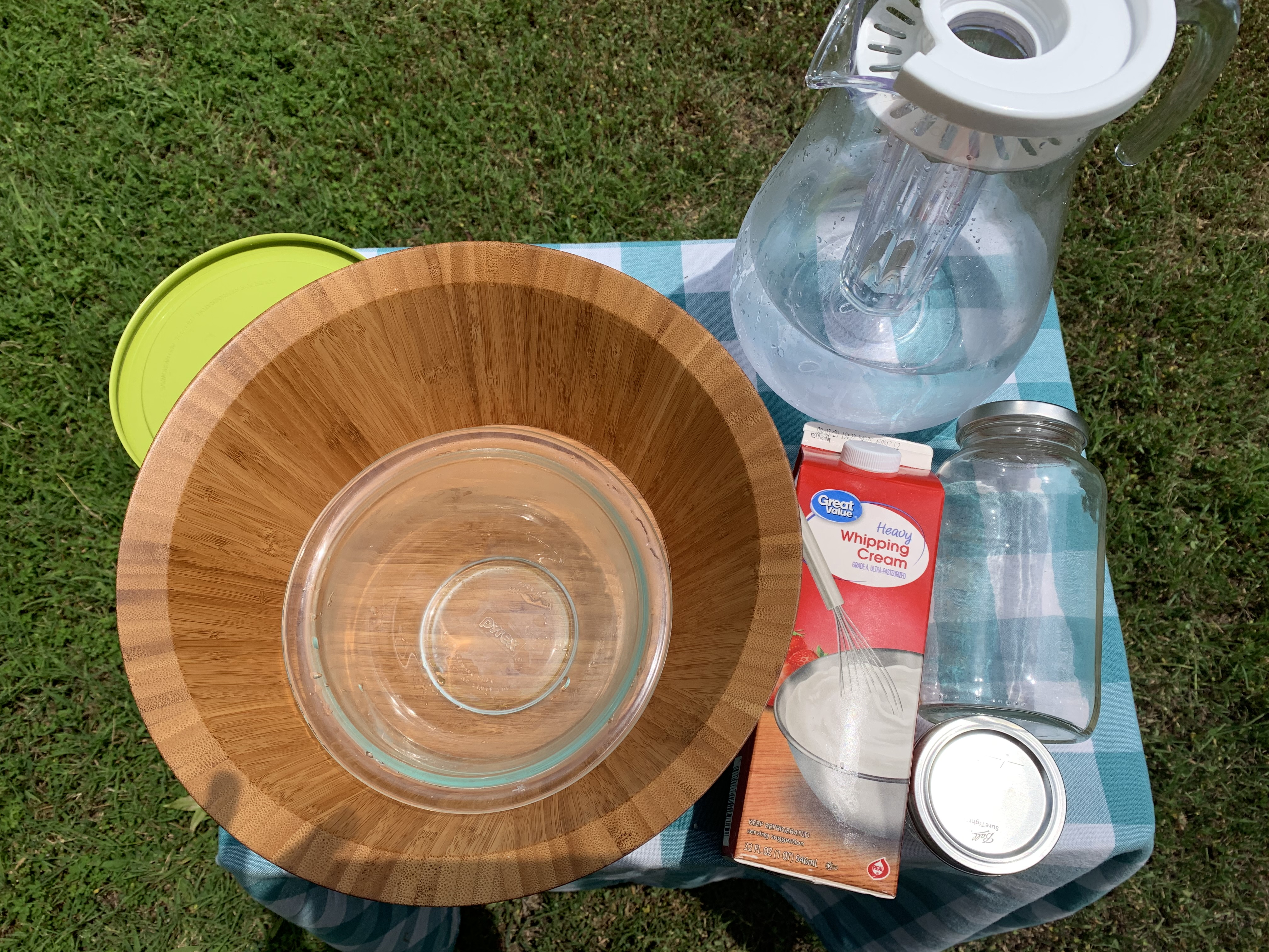 On a table sits all the materials needed for the activity: mason jar, heavy whipping cream, two containers (one for buttermilk and one for the butter), a bowl and a pitcher of cold water.)