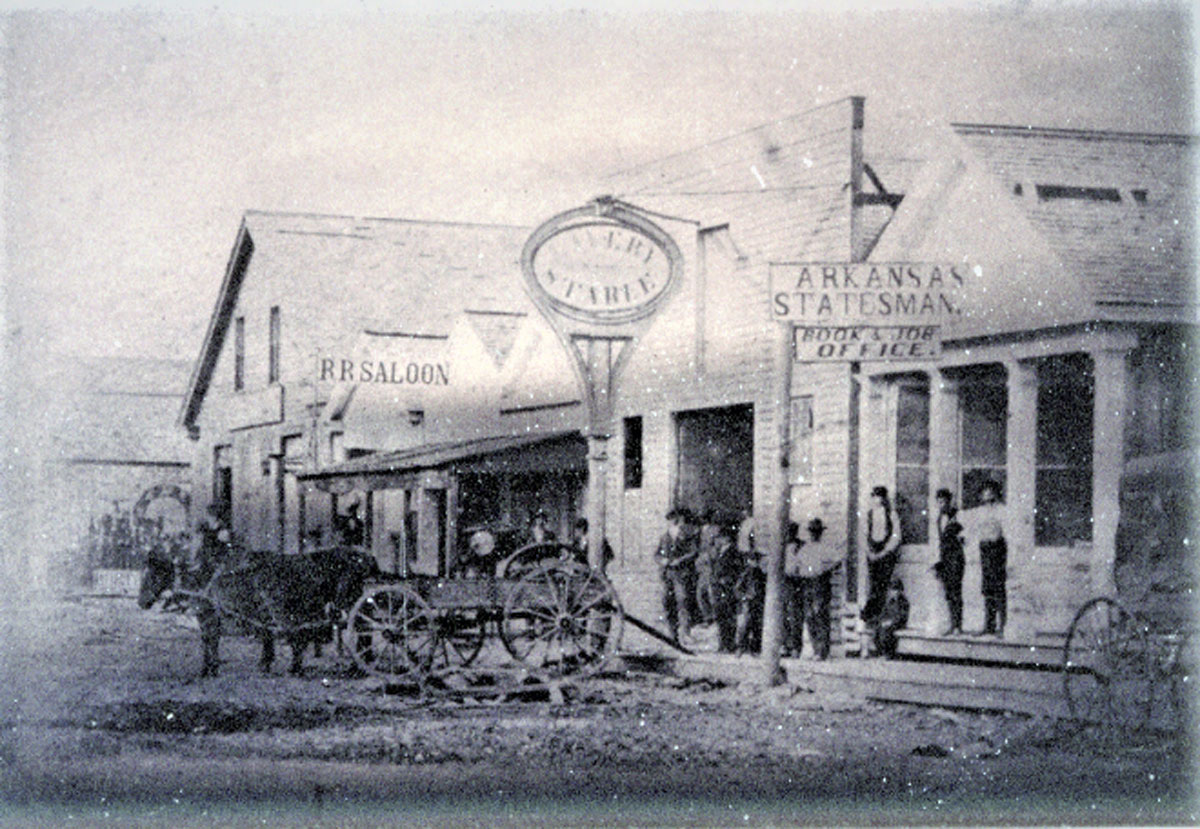 a black-and-white historic picture of a row of wooden buildings with a horse and buggy standing in front of them