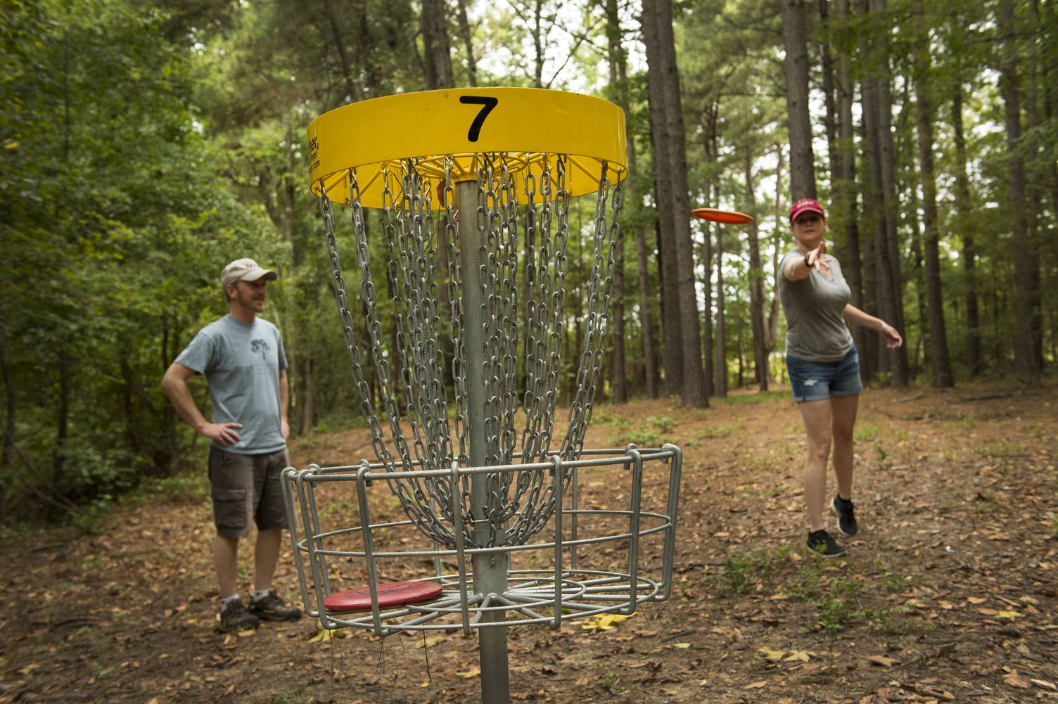 Woman standing behind disc golf basket while tossing a disc into it, man standing beside her watching 