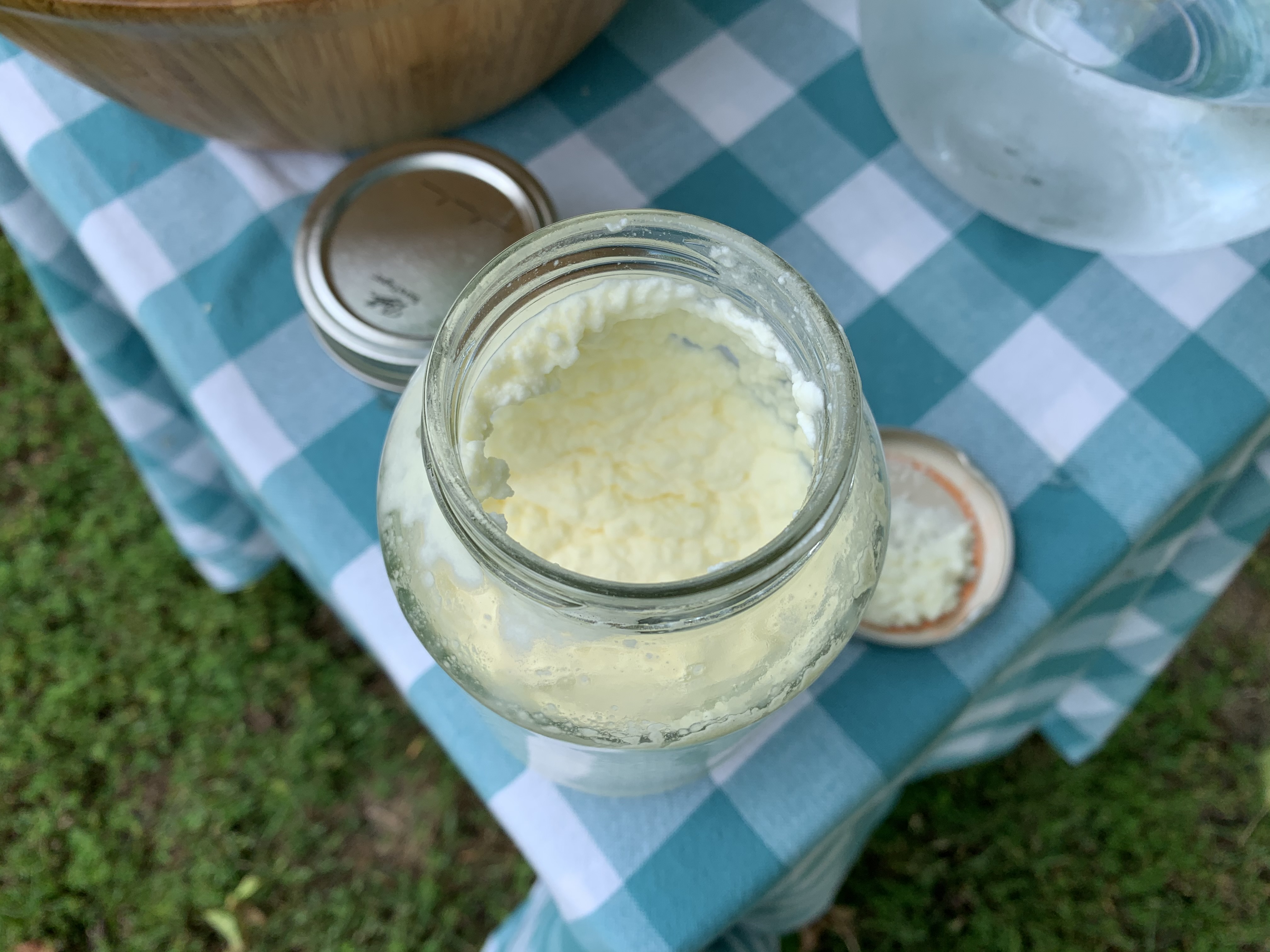 On a table there is a mason jar filled with cream that has the texture of ricotta cheese.