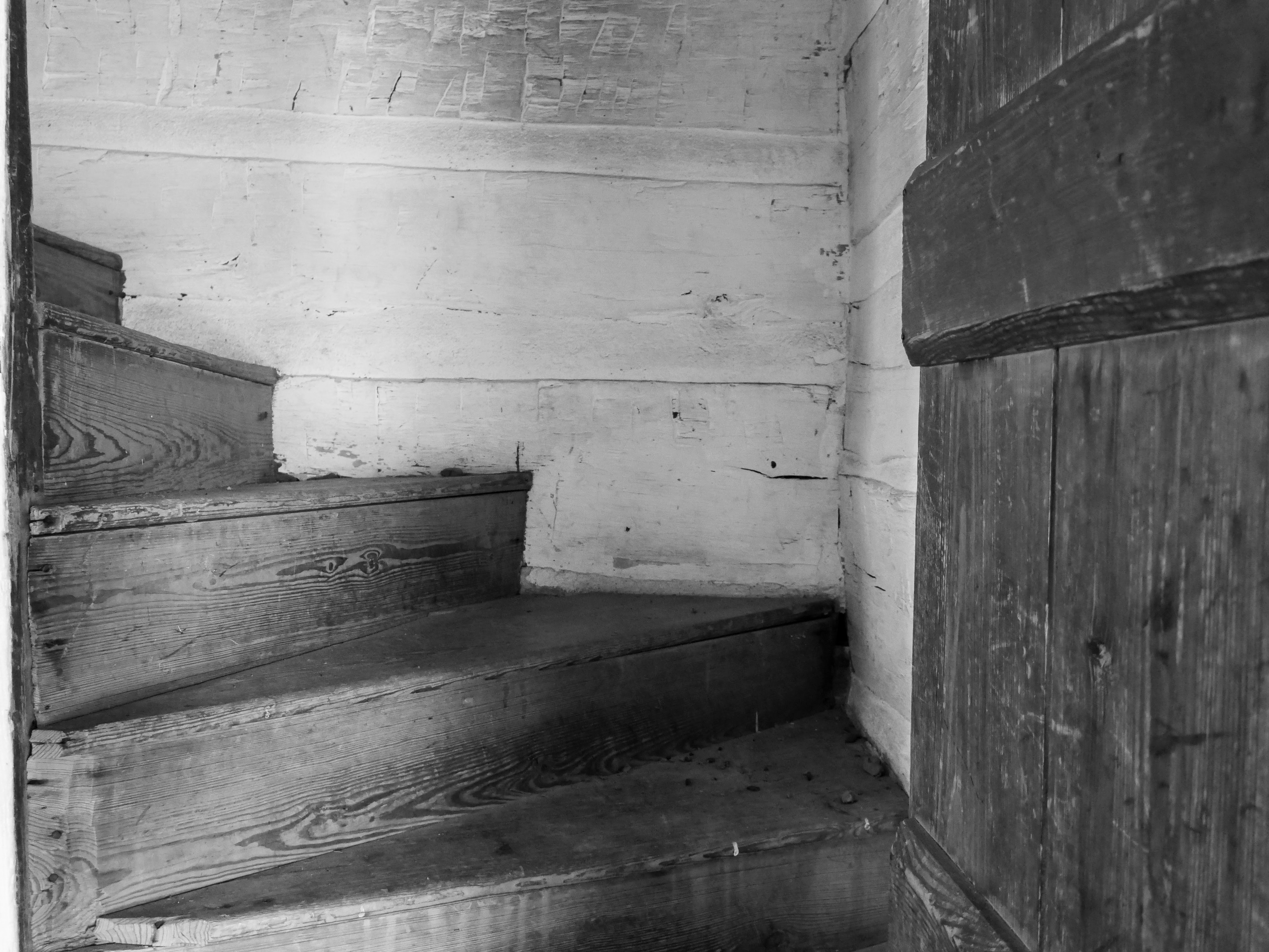 Through a wooden doorway, steep unpainted wooden stairs turn sharply to the left.