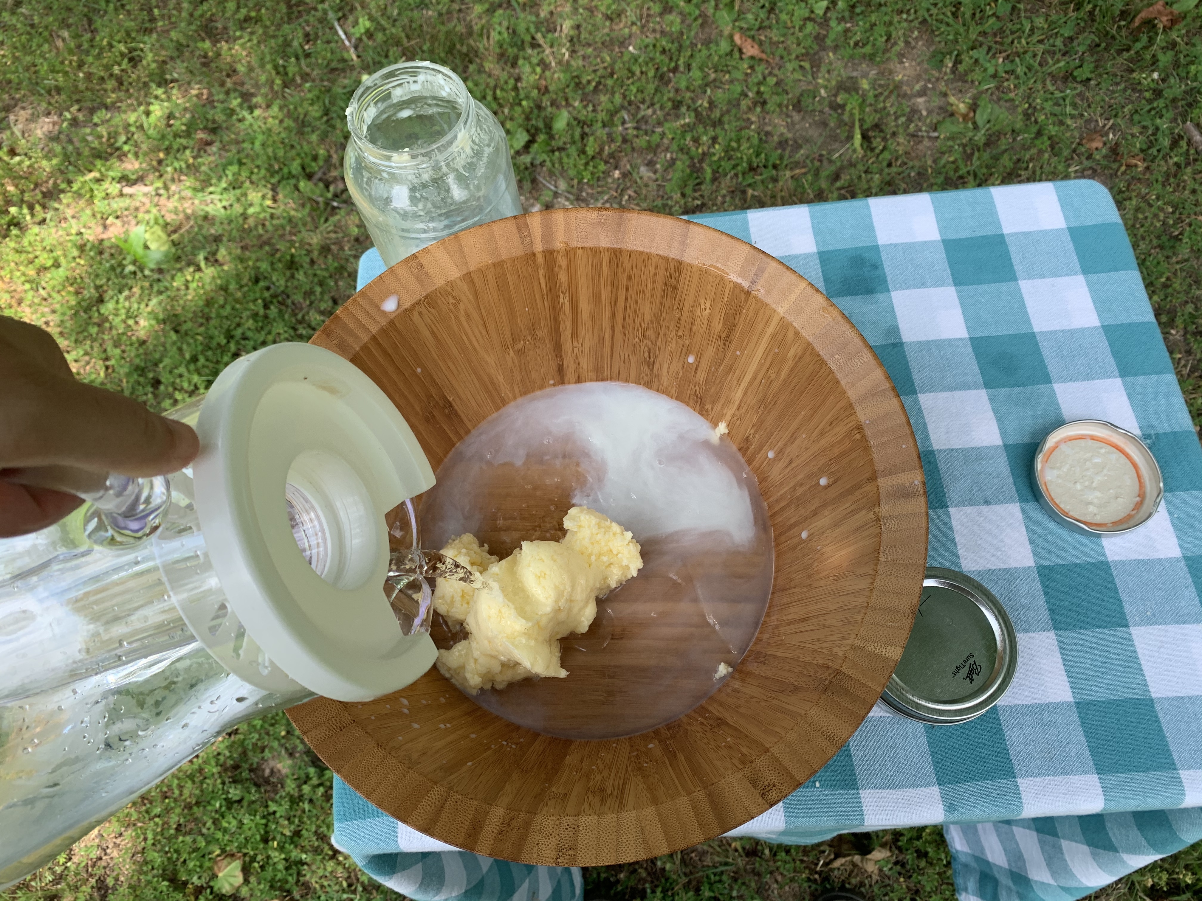 : Water is being poured over butter that is in a bowl on a table. The liquid coming off the butter is cloudy