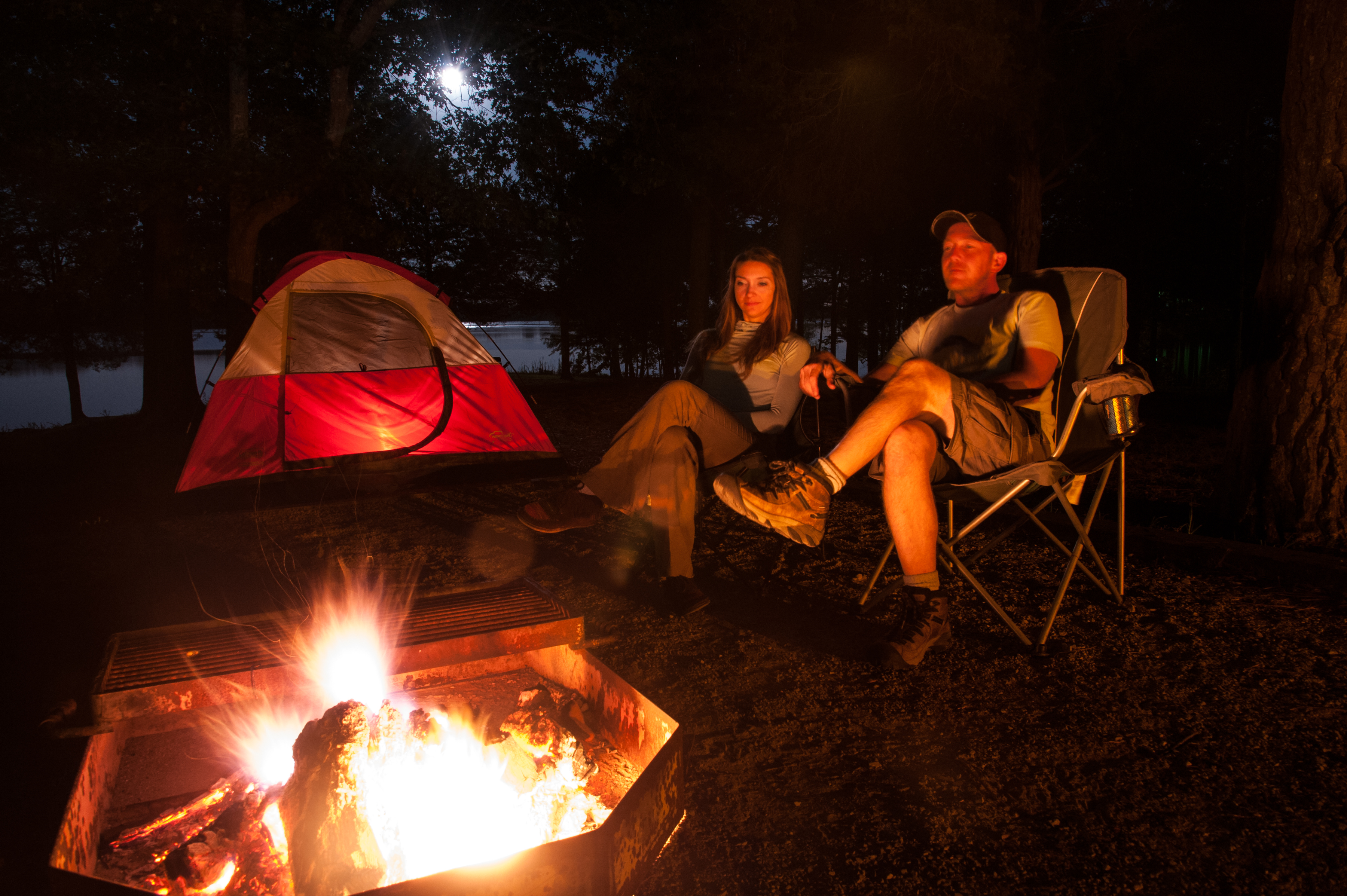 A couple sitting in chairs beside a campfire