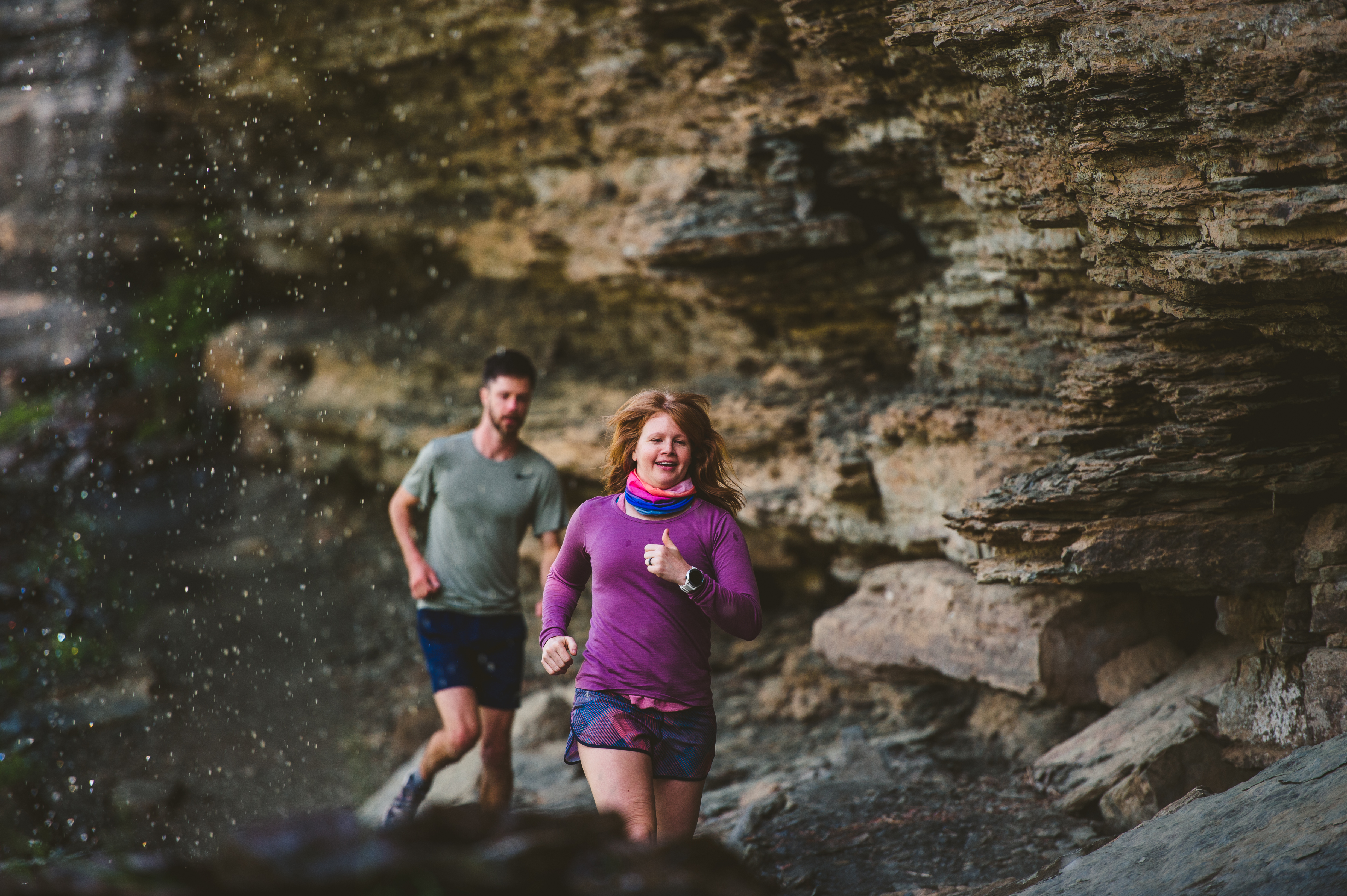 A man and a woman trail running under a waterfall at Devil's Den State Park