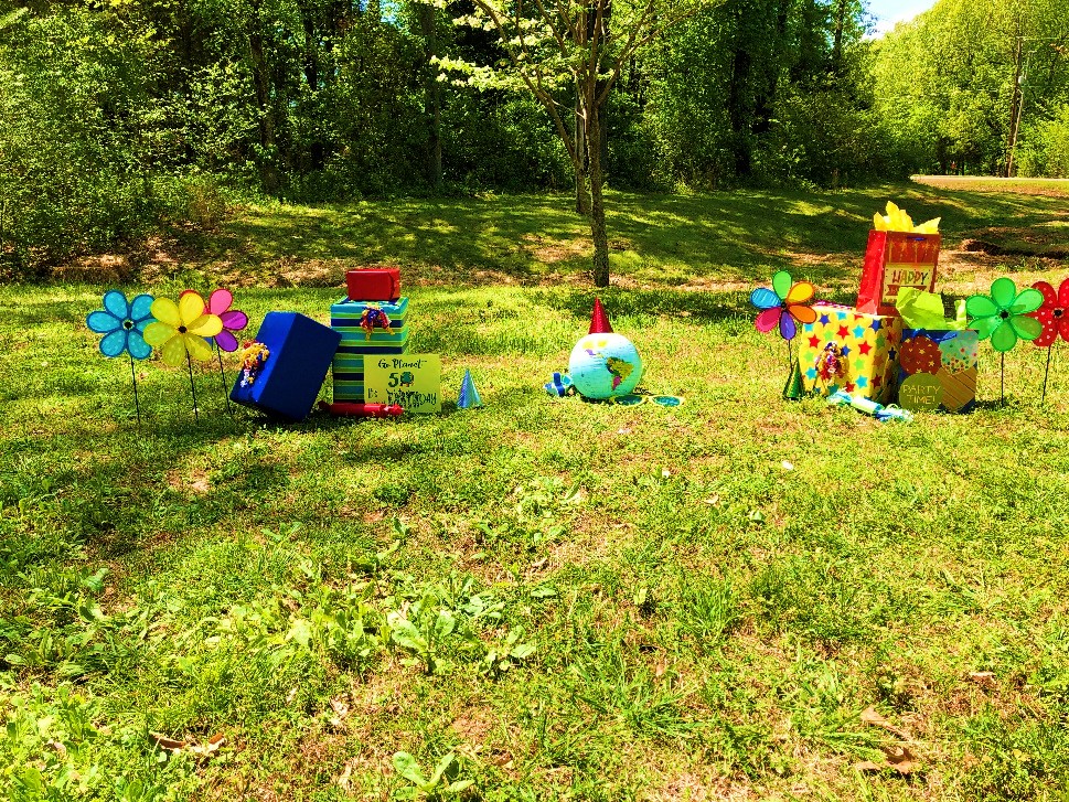 Green grass foreground with globe and brightly colored yard and party decorations, forested background
