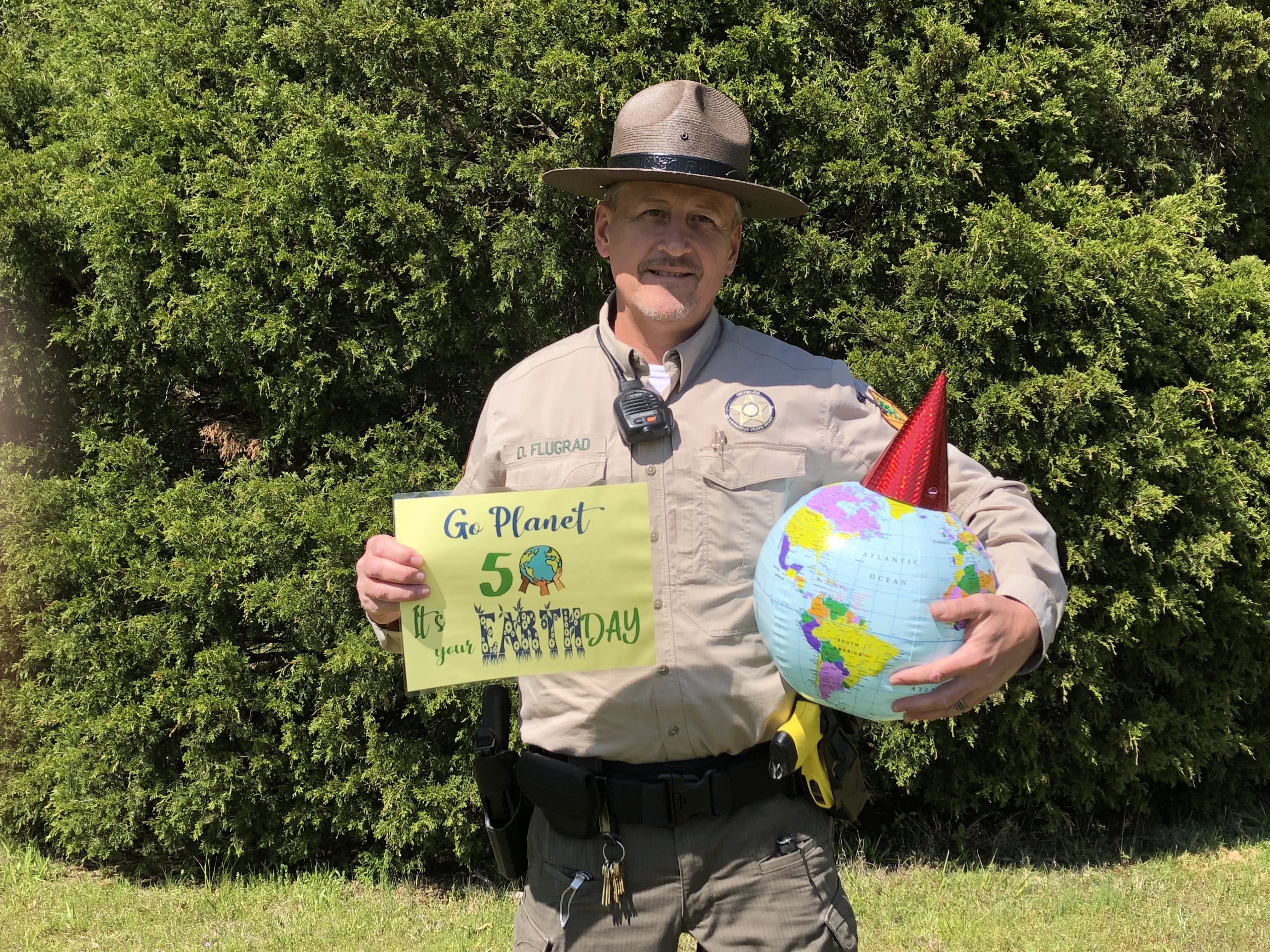 Park ranger in uniform holding globe and sign saying, “Go Planet, It’s Your 50th Earth Day.”