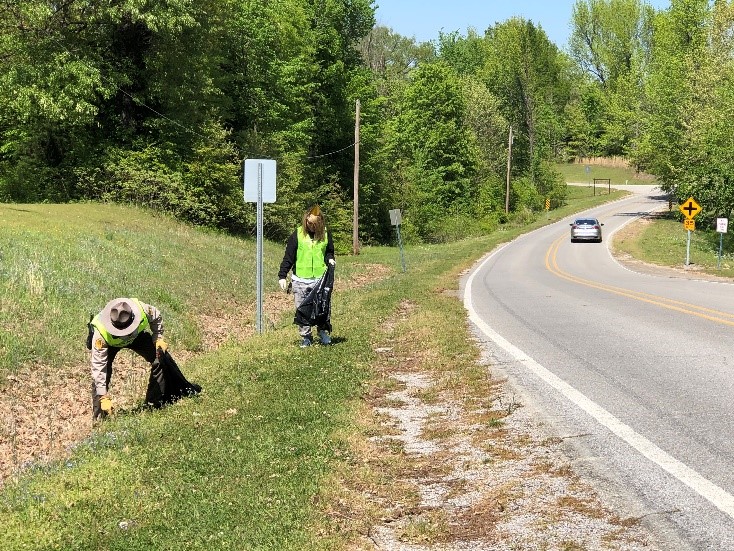 Park ranger and volunteer in yellow safety vests picking up litter along road