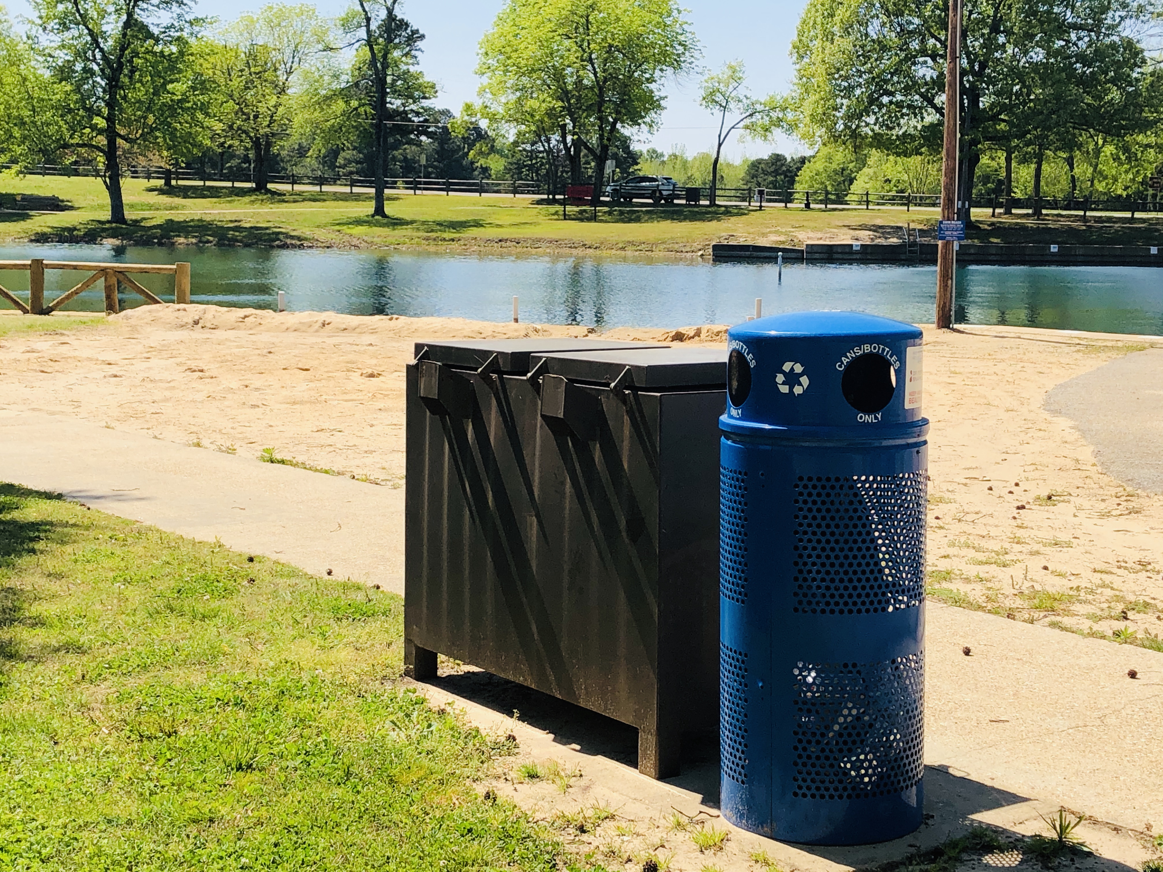 nother blue, metal recycling bin in the foreground with Lake Ponder swim beach in the background 