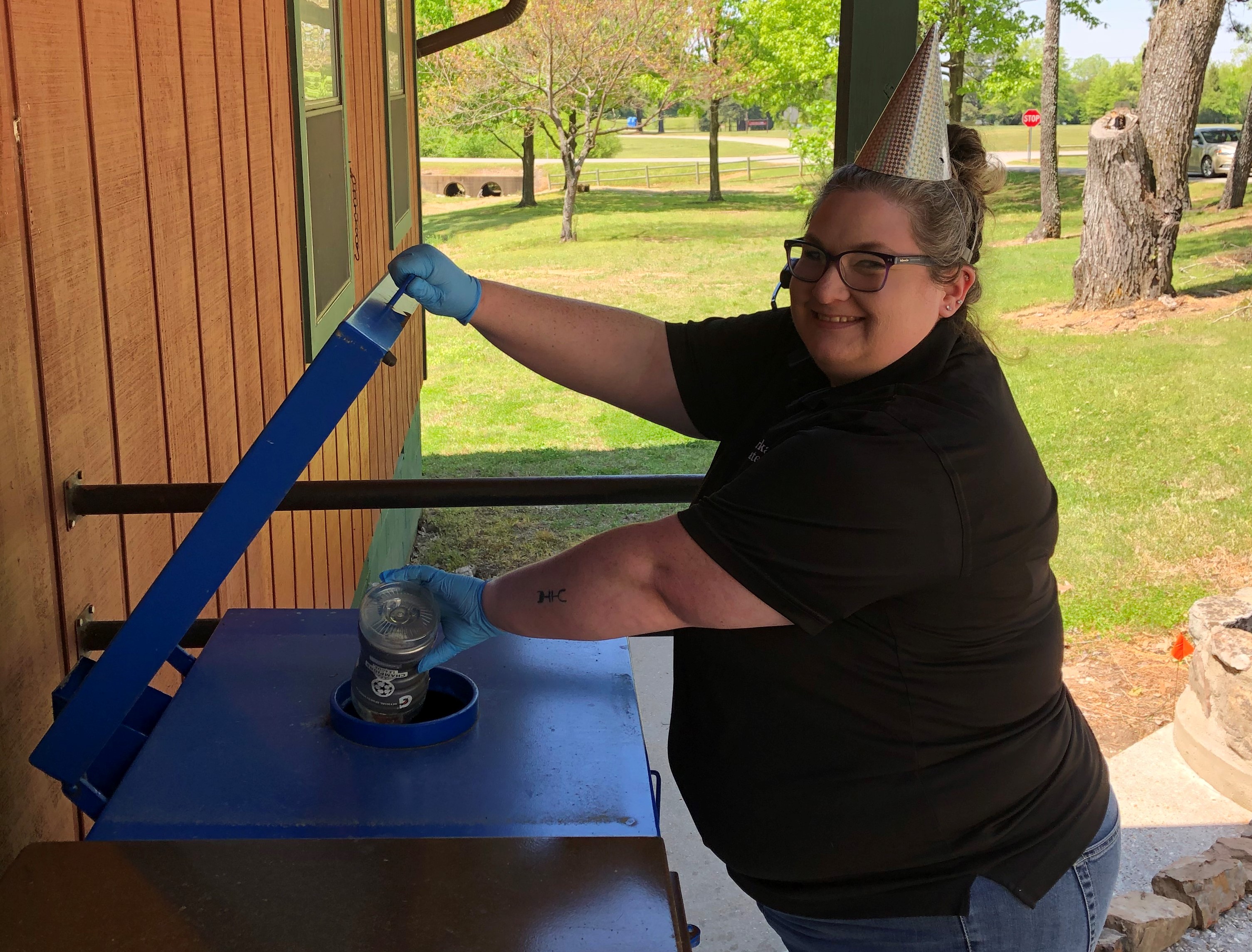 Park employee smiling, wearing party hat, place bottle in recycling bin