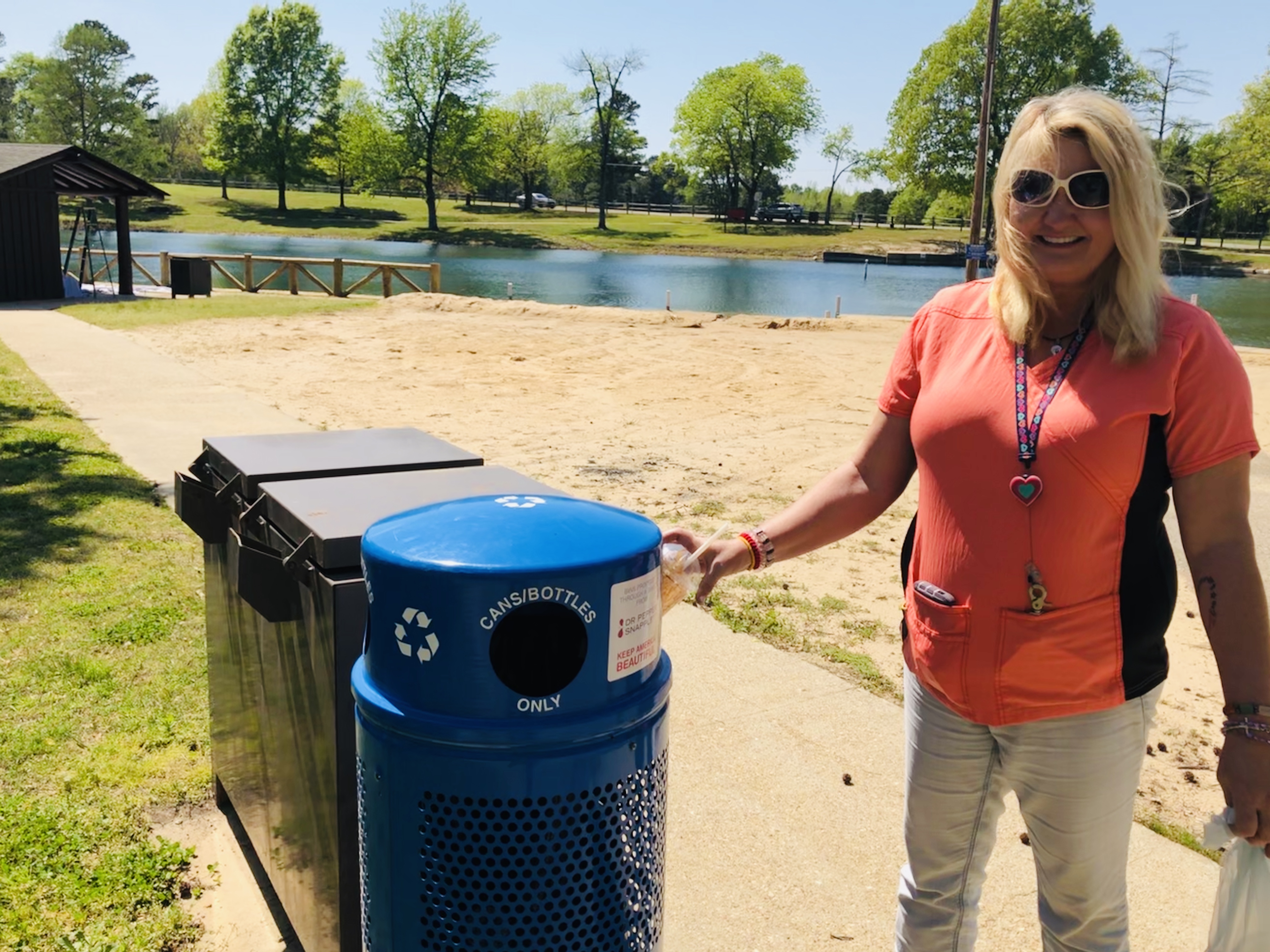 Female staff member dropping a plastic cup into a blue recycling bin after finding it at Lake Ponder beach 