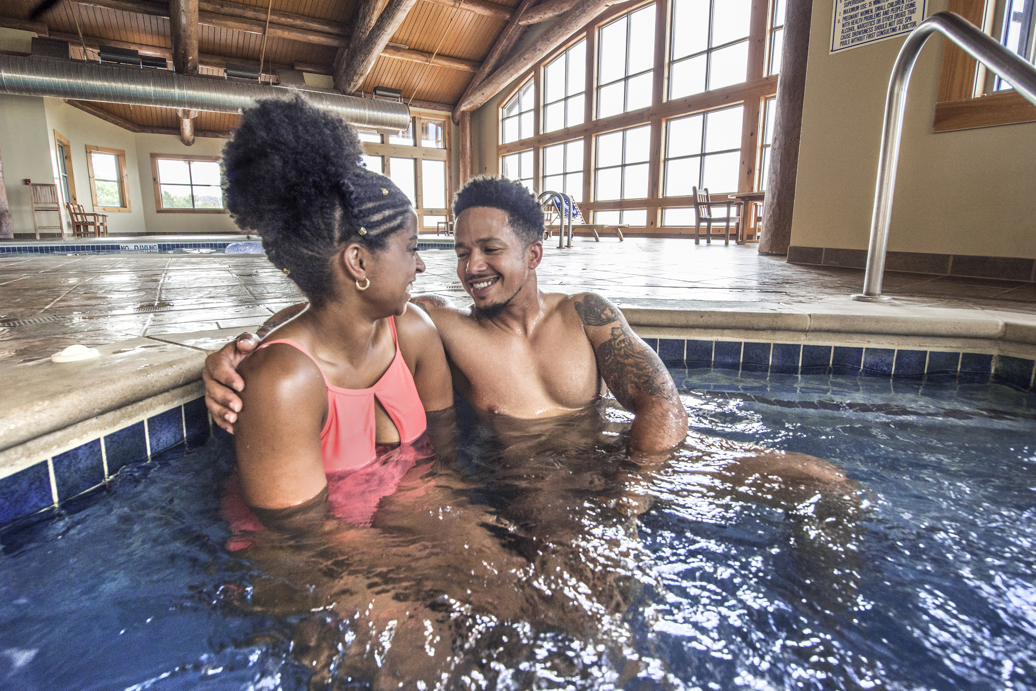 Couple sitting in hot tub with swimming pool in the background inside the lodge at Mount Magazine State Park