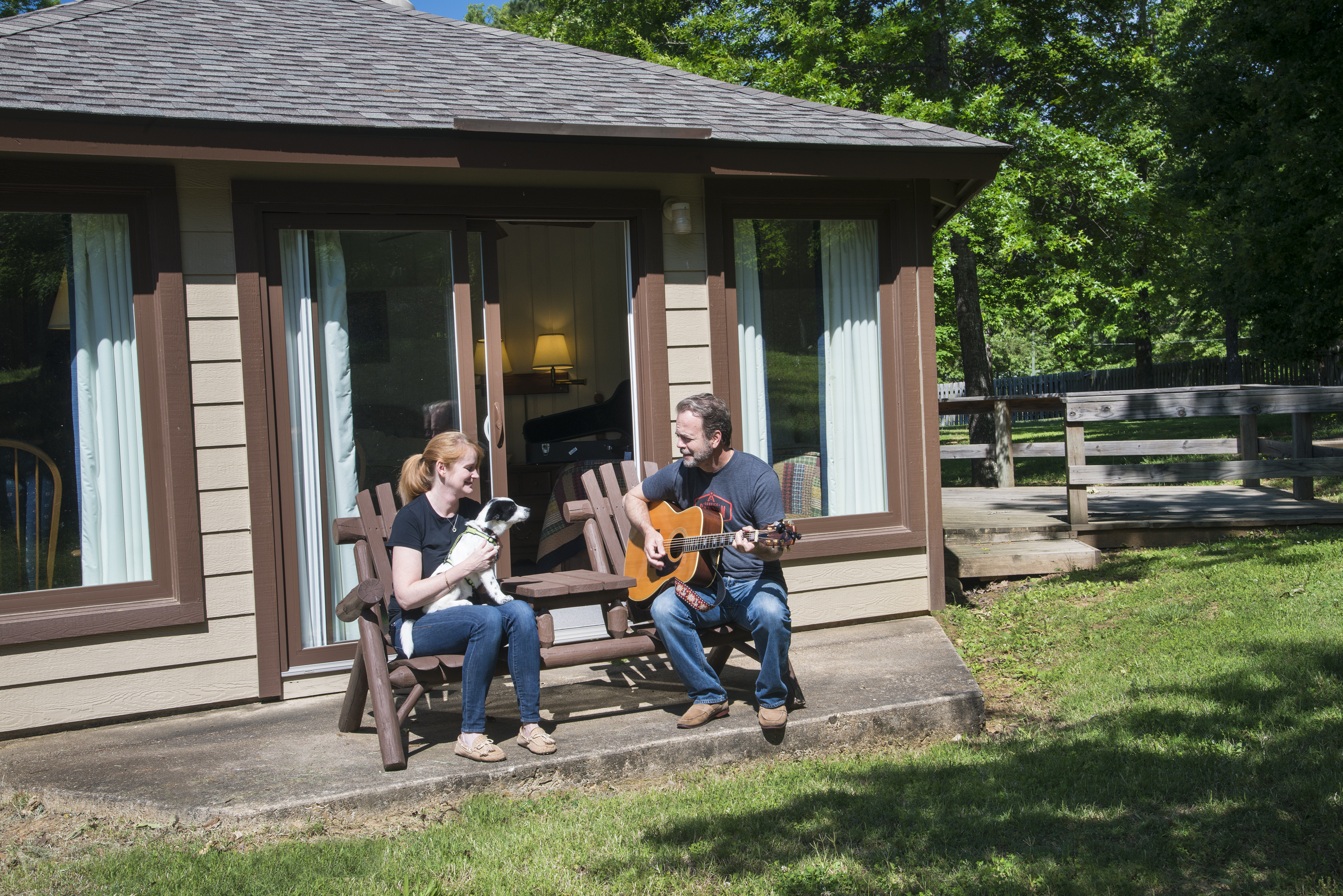 Couple sitting outside cabin at Ozark Folk Center State Park playing guitar and holding a dog