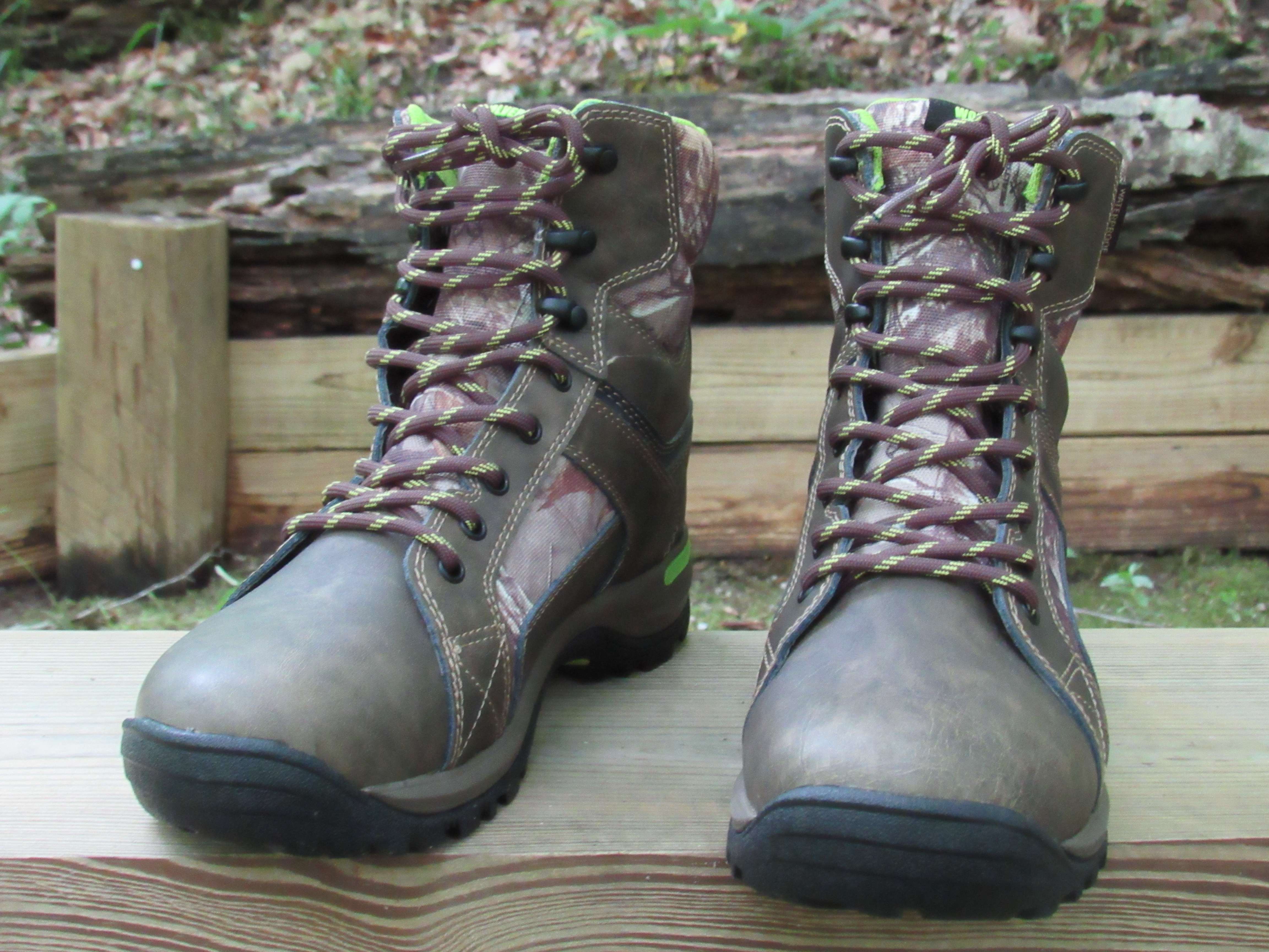 Brown hiking boots resting on a bench in front of a wooden fence.