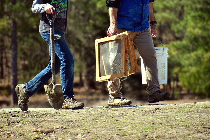 Two people carrying a screen and shovel to search for diamonds