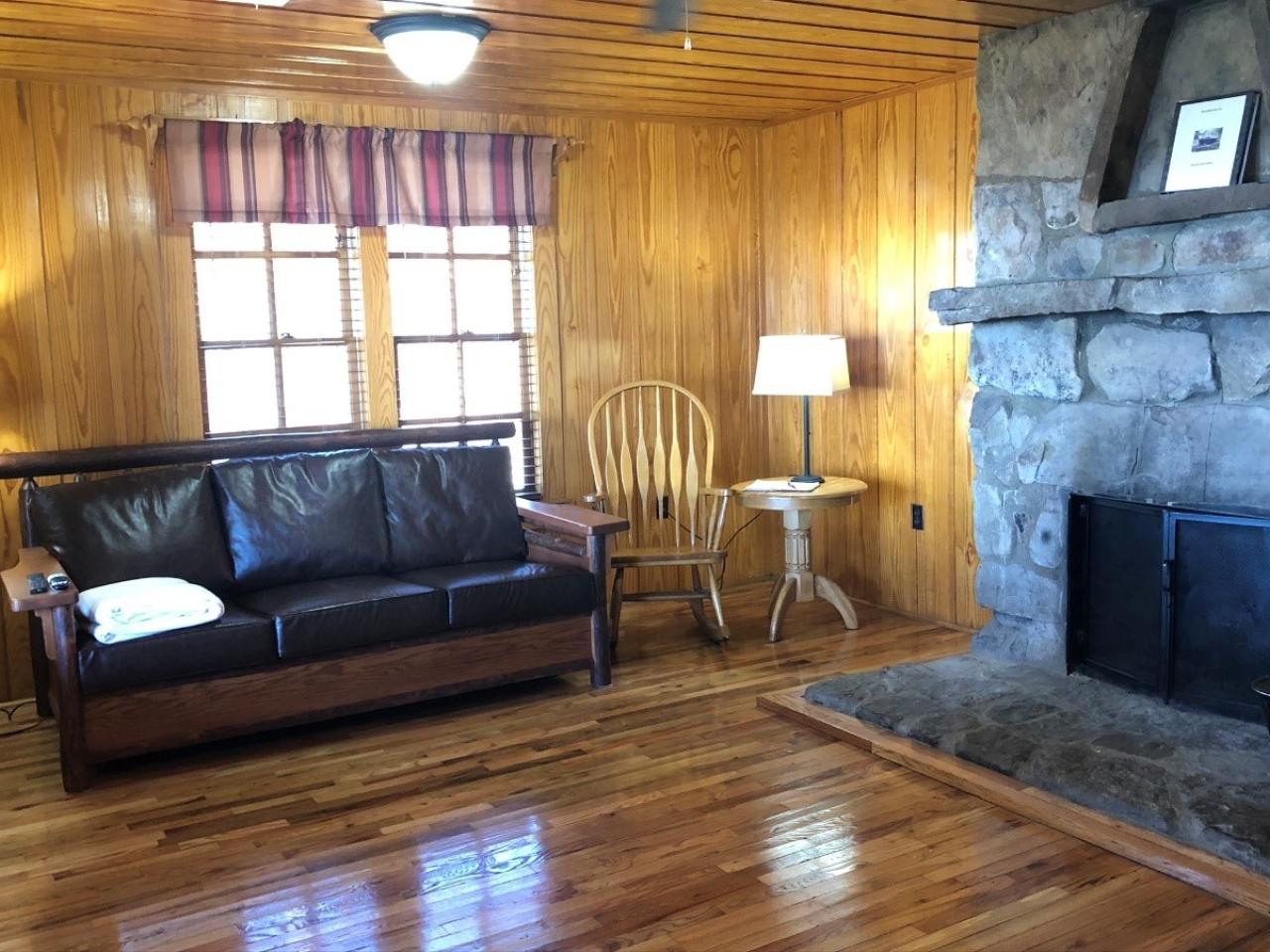 A view of the living room in Cabin 2, which includes a couch, rocking chair and stone wood burning fireplace