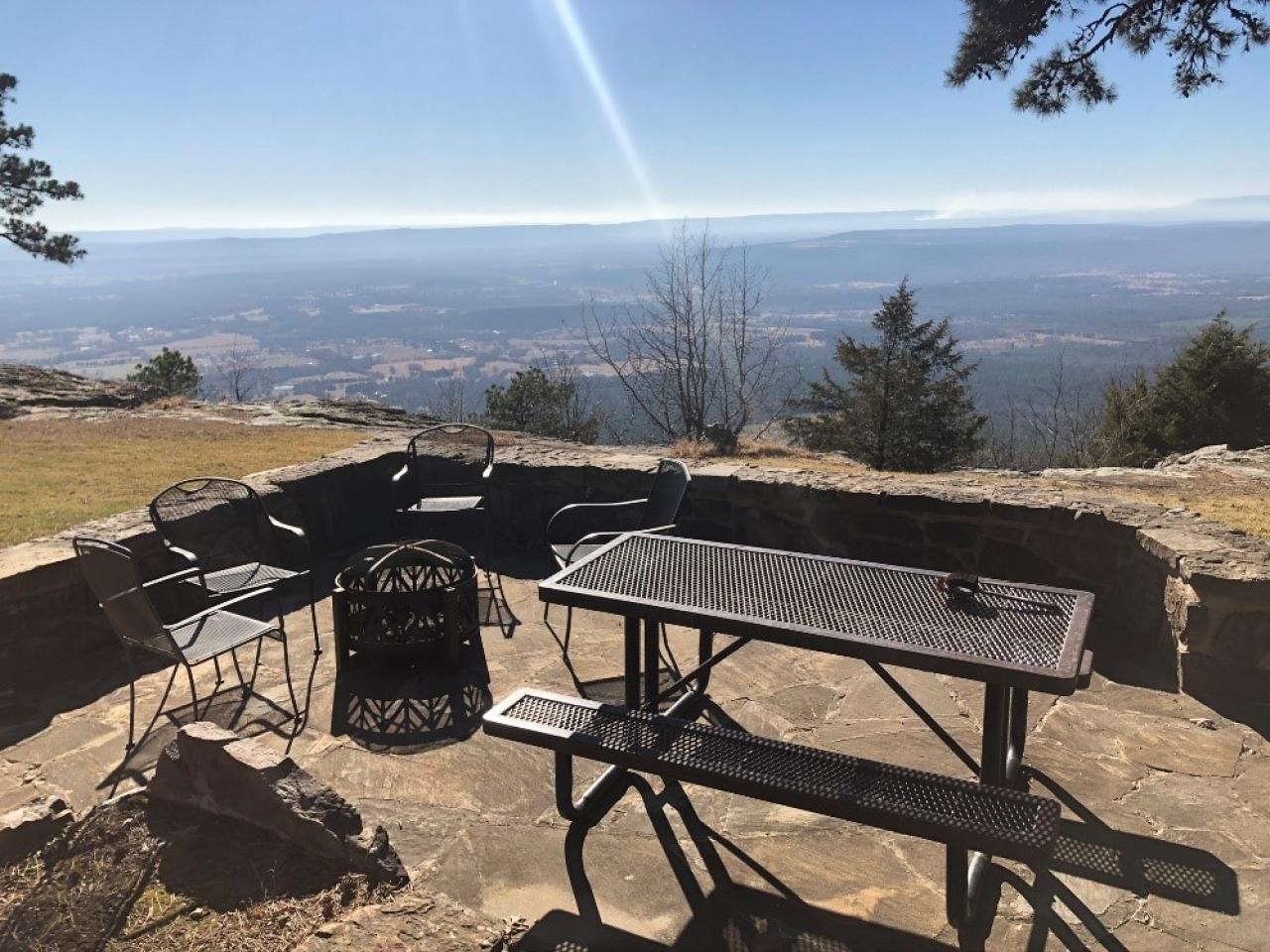 A view of the outdoor seating at Cabin 2, which includes a picnic table, four chairs, a fire pit and beautiful view overlooking the river valley below