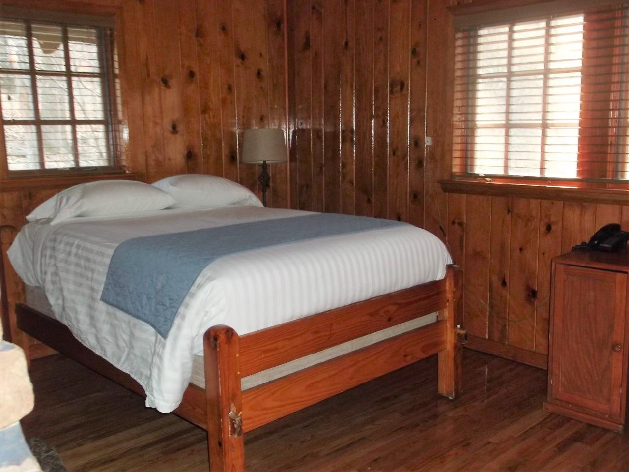 A view of the bedroom in cabin 18 including a bed, side table and two exterior windows