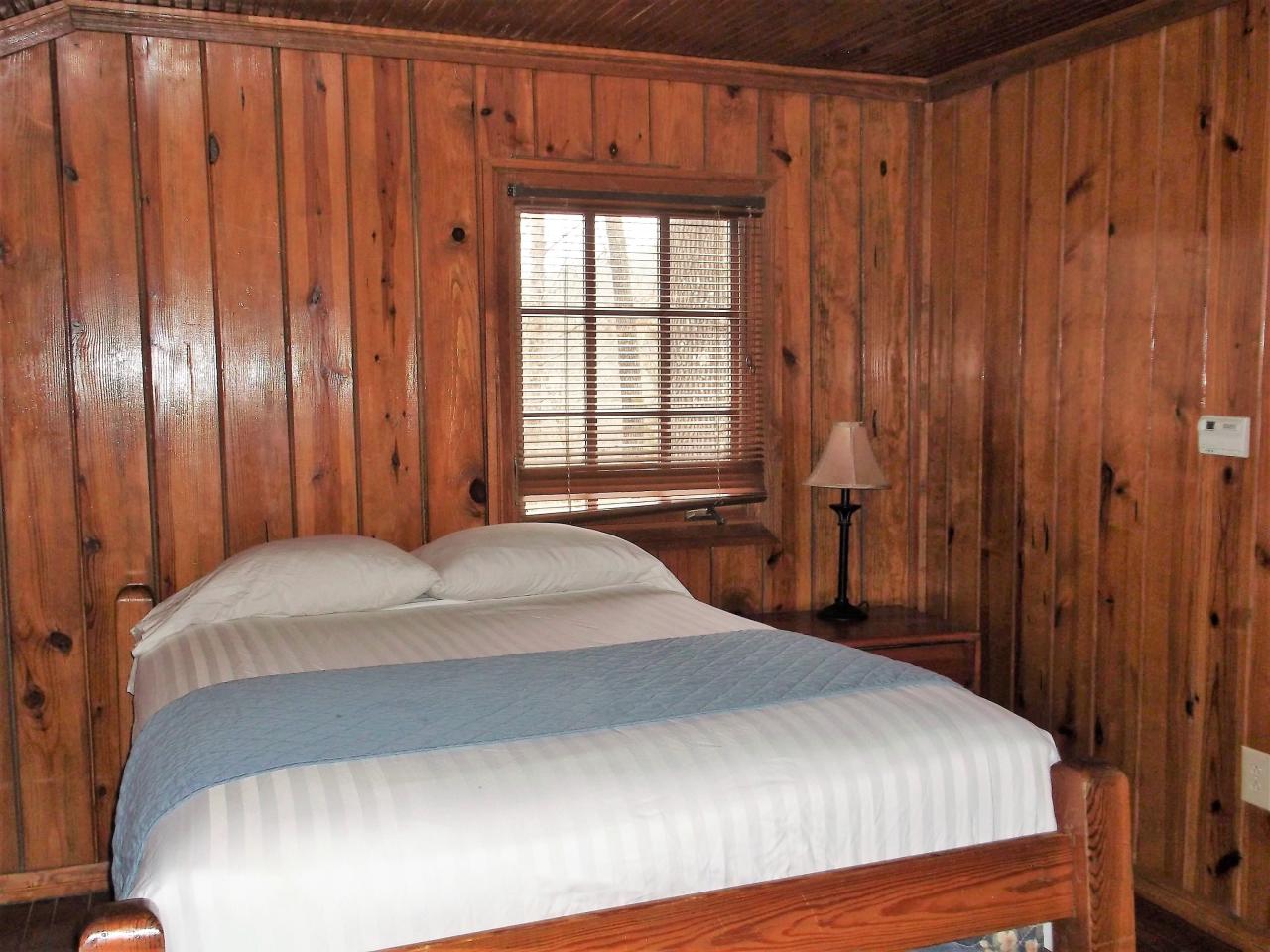 A view of one of the 3 bedrooms in Cabin 7 including a bed, a side table and an exterior window