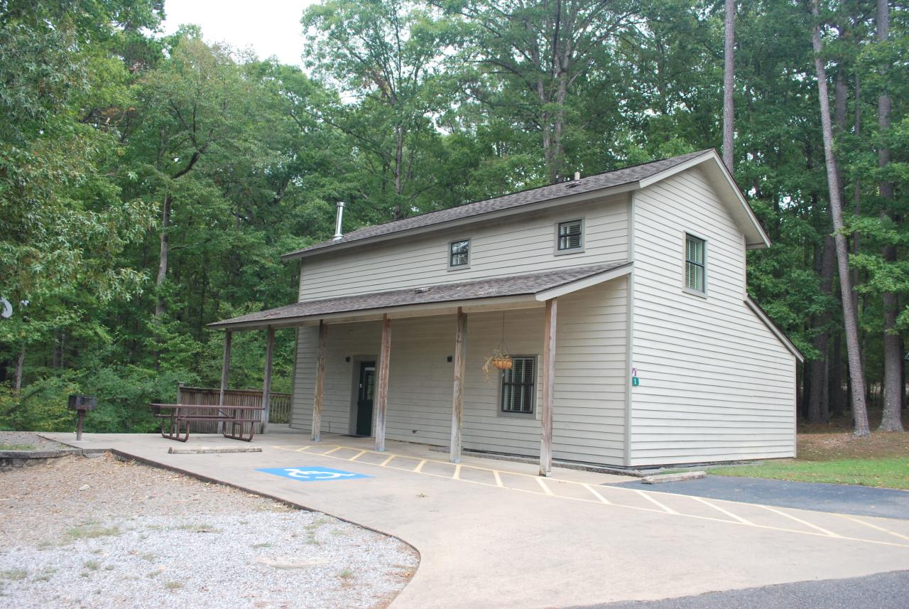 The exterior view of the two-storied Cabin 1 at Lake Ouachita State Park including a parking space and outdoor seating area with picnic table and grill