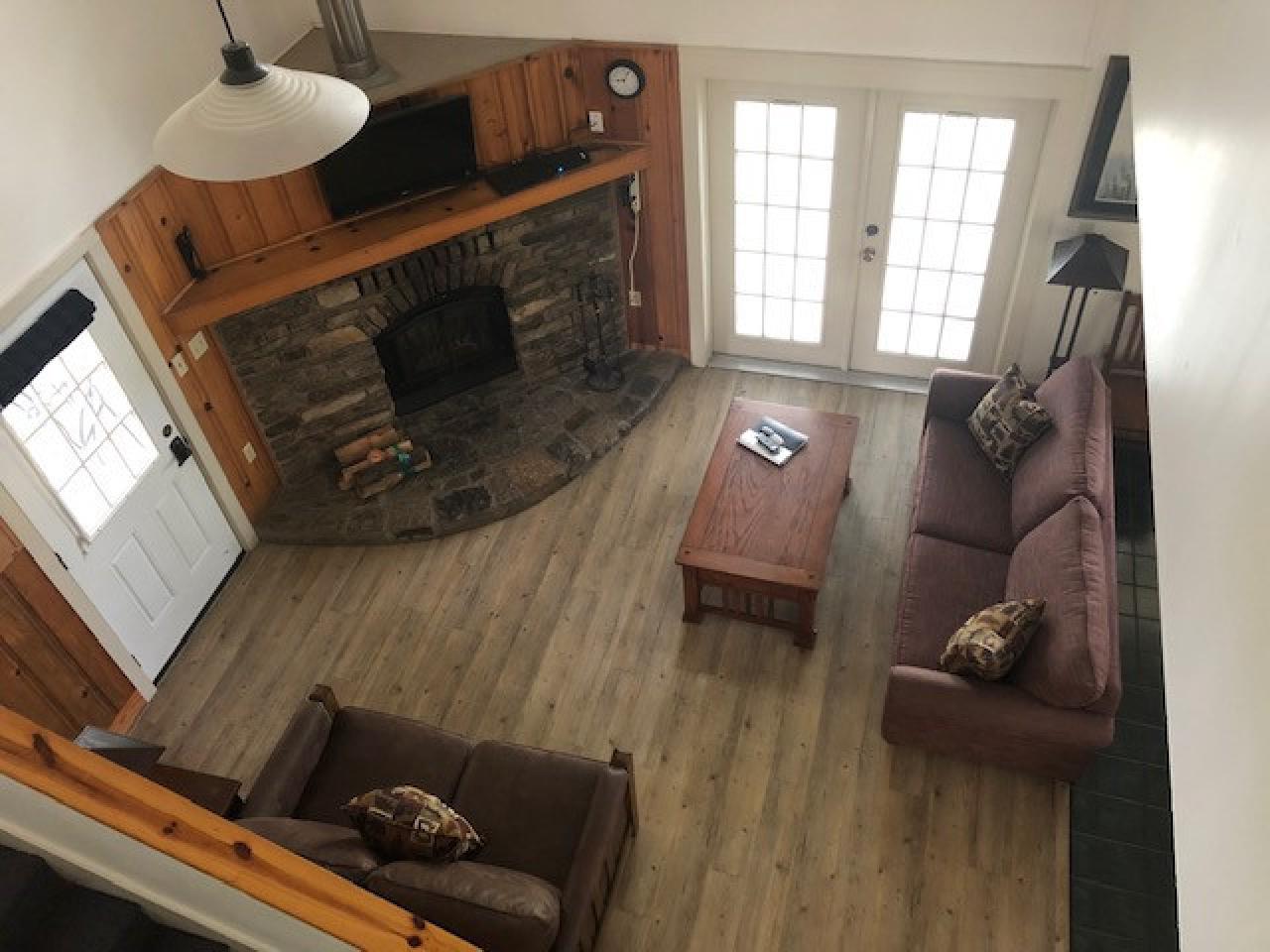 A view of the living room seating area in Cabin 1 at lake Ouachita State Park from the second story including two couches, a coffee table, a fireplace and french doors that lead to the outside