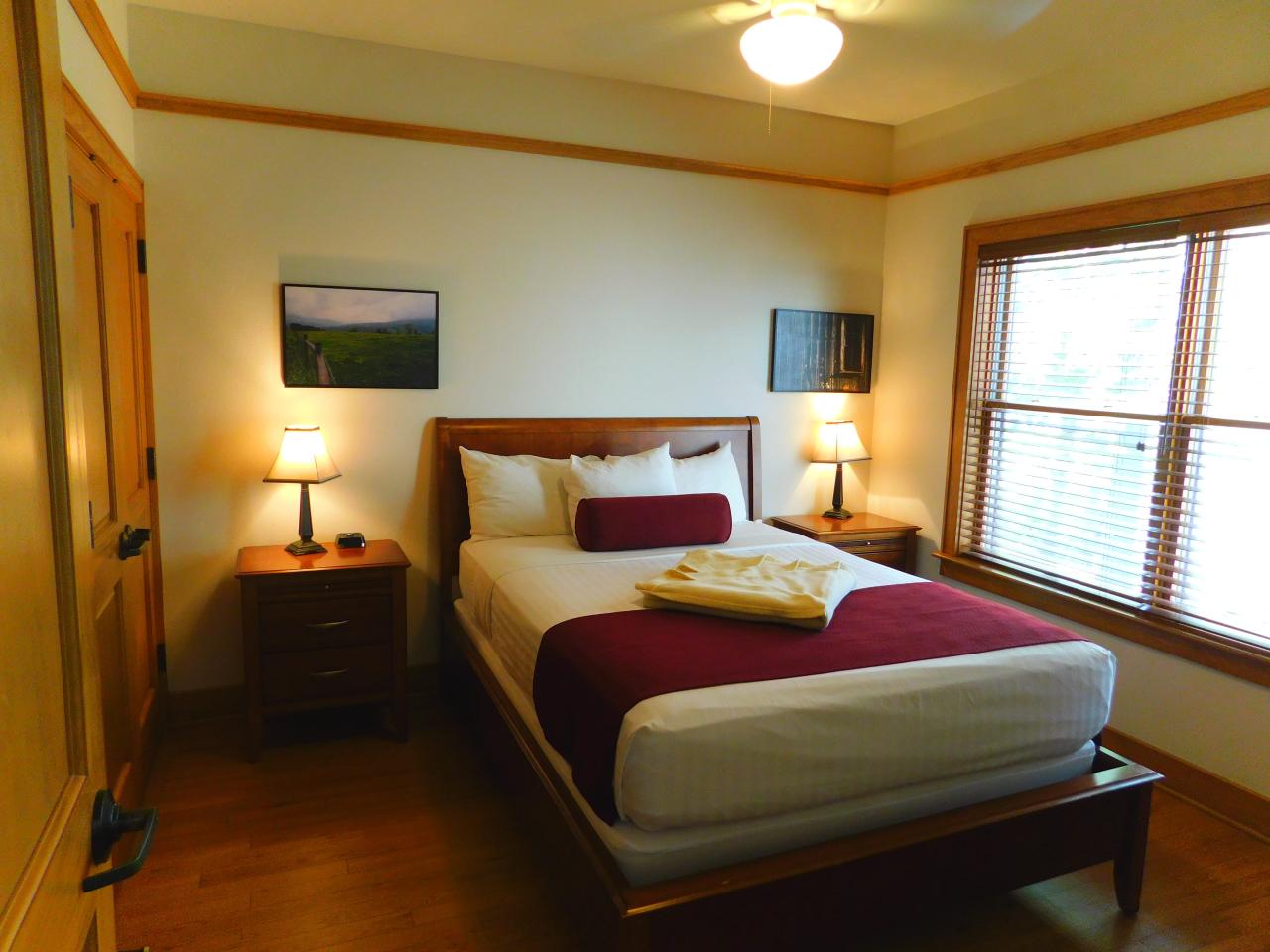 A view of one of the bedrooms at Cabin 3 at Lake Ouachita State Park including a bed, 2 side tables and a large exterior window