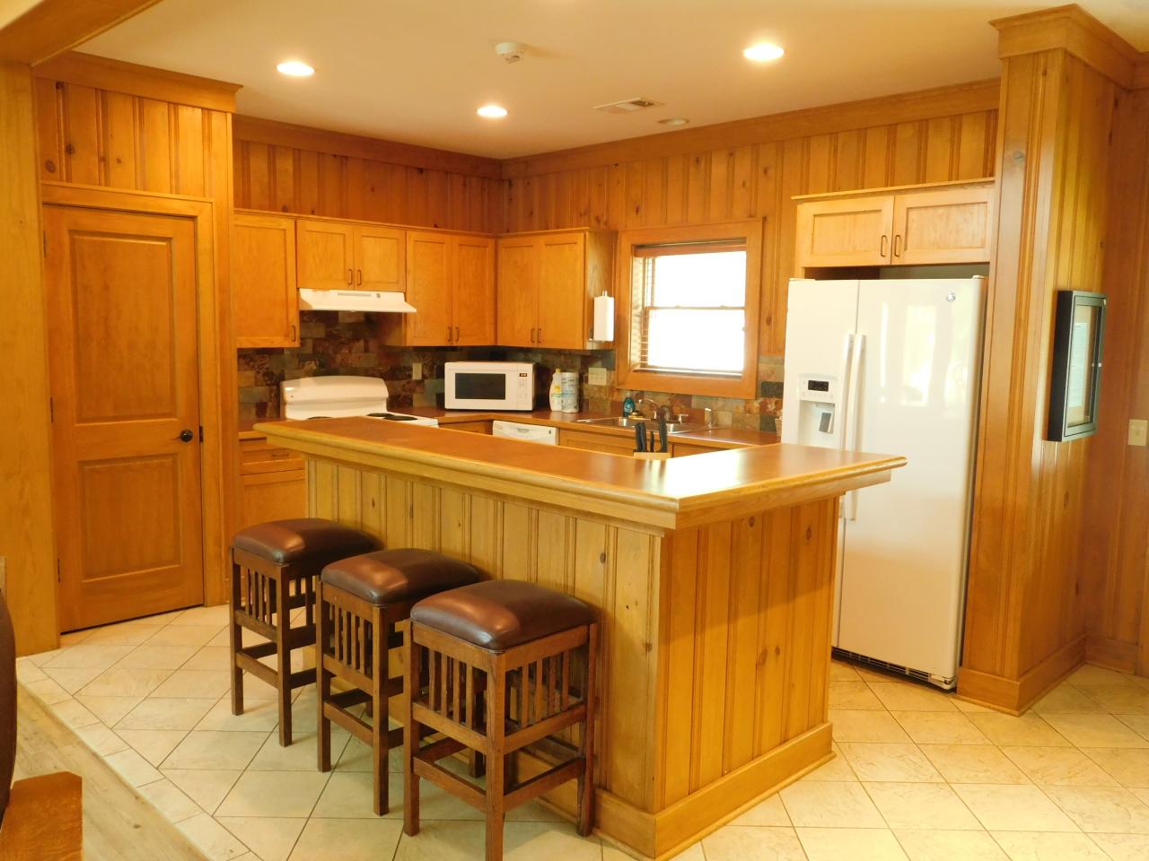 A view of the full kitchen at Cabin 3 at Lake Ouachita State Park including a fridge, dishwasher, oven, microwave and kitchen island with seating