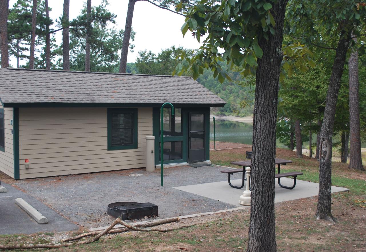 An exterior view of Camper Cabin 59 at Lake Ouachita State Park including parking spaces and an outdoor seating area with a picnic table and grill