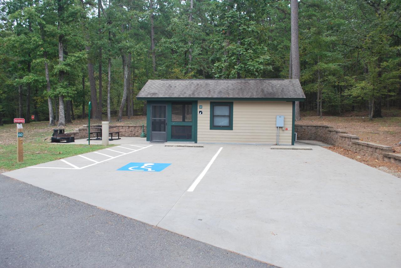 An exterior view of Camper Cabin 60 at Lake Ouachita State Park including parking spaces and an outdoor seating area with a picnic table and grill