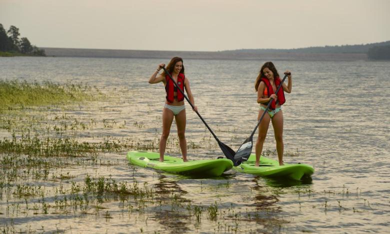 Two girls stand up paddle boarding on a lake at dusk
