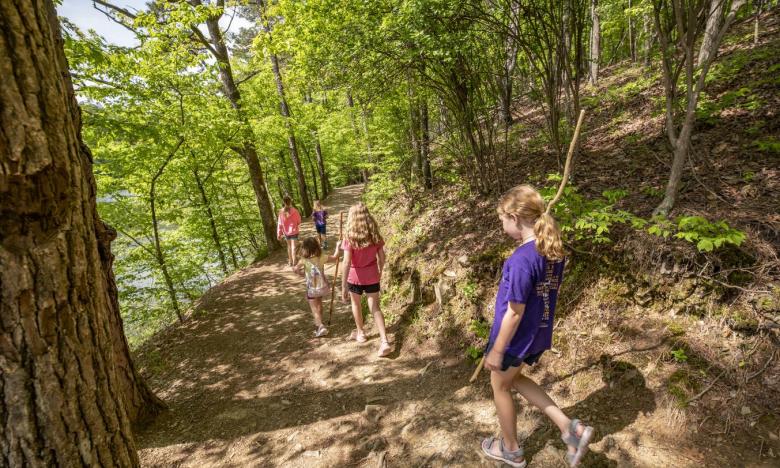A group of girls hiking downhill away from the camera on a wooded trail at Lake Catherine