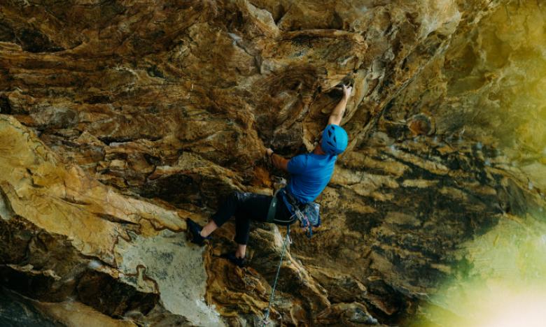 A man lead climbing on an overhang wall reaching for the next hold. 
