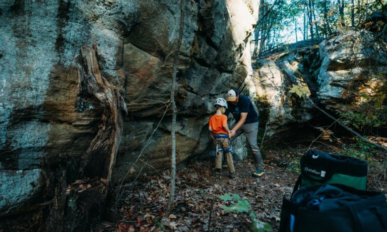 A man checking the harness of a small child before climbing. 