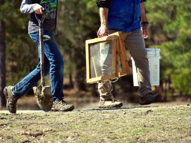 Two people carrying a shovel and screens to search for diamonds