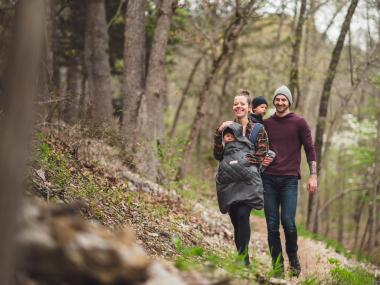 Family hiking at Hobbs State Park-Conservation Area in the fall. Mom has baby in front carrying backpack and the dad is carrying another small child.