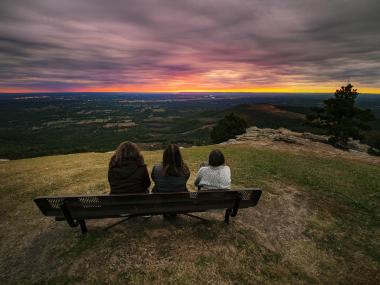Three women sitting on a bench watching a sunrise at Mount Nebo State Park