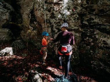 A woman and small child top roping a rock wall share a fist bump at the bottom.
