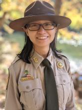 Pearl Jangjiravat smiling, wearing her uniform and campaign hat with water and trees in the background