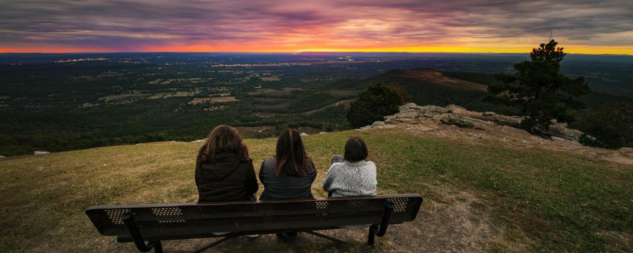 Three women sitting on a bench watching a sunrise at Mount Nebo State Park