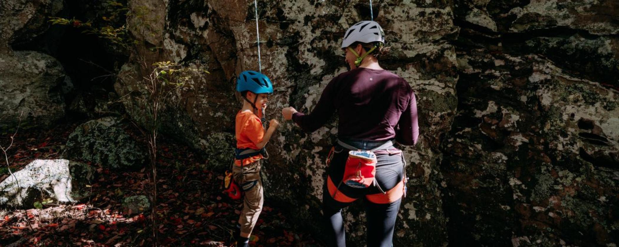 A woman and small child top roping a rock wall share a fist bump at the bottom.