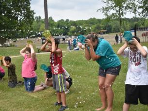 People holding a container on their head while their teammate tries to squirt water in it