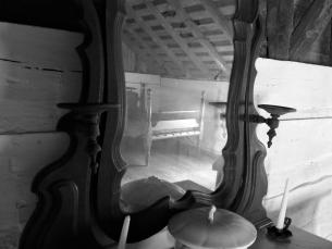 An ornate dresser with large mirror reflects a wooden bed. Two candles and a covered bowl set atop the dresser.