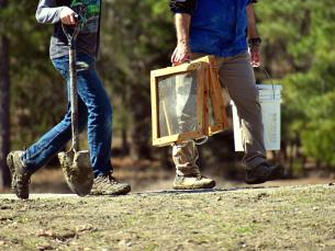 Two people carrying a shovel and screens to search for diamonds