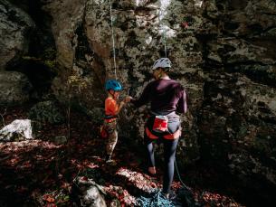 A woman and small child top roping a rock wall share a fist bump at the bottom.