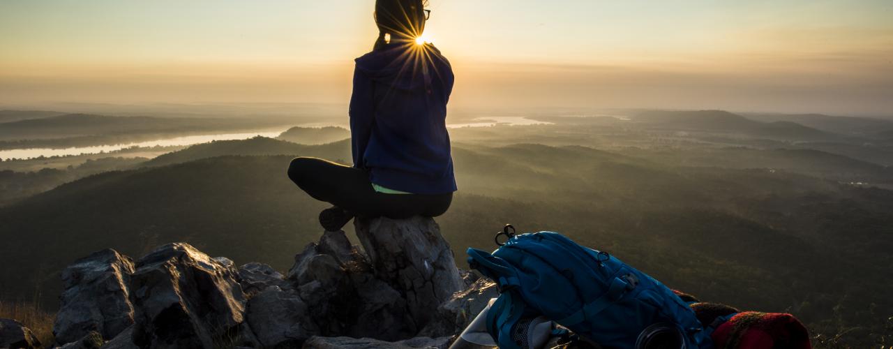 Hiker sitting on top of Pinnacle Mountain State Park looking at sunset