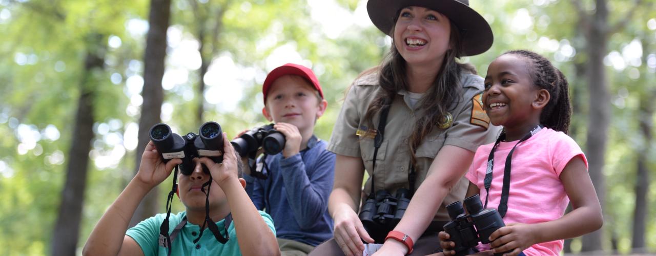 Park interpreter sitting with children learning how to birdwatch