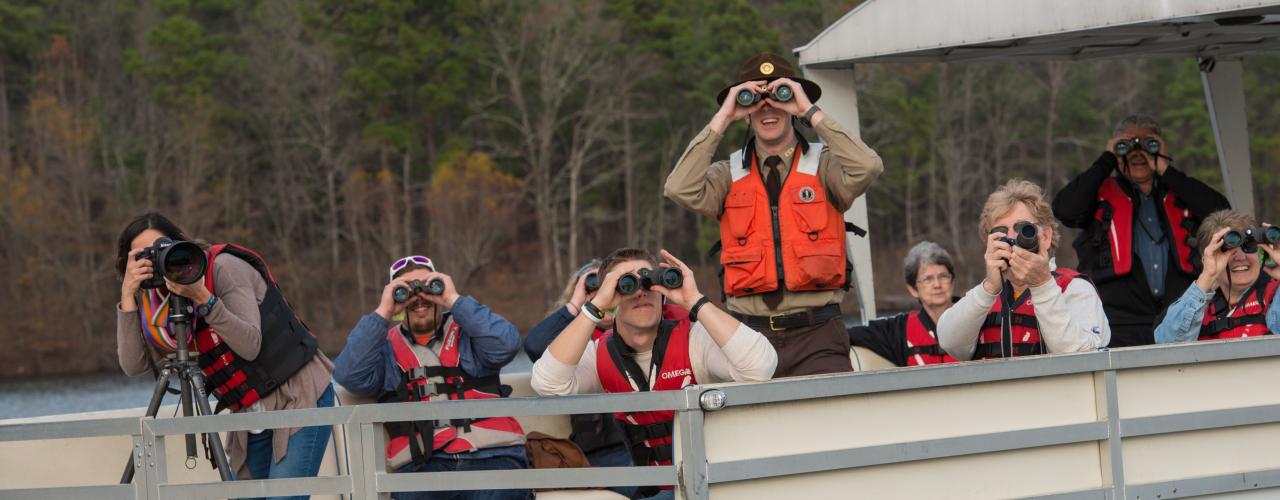 Park interpreter leads a group on a boat tour as they look through binoculars for local birds and wildlife